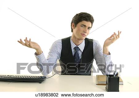 Stock Image - Portrait of a businessman sitting at a desk and shrugging in an office. Fotosearch