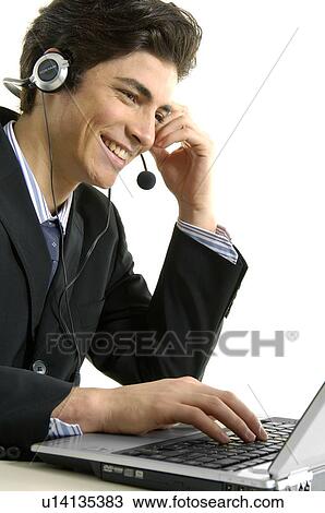 Stock Image - Side profile of a businessman wearing headset and using a laptop. Fotosearch