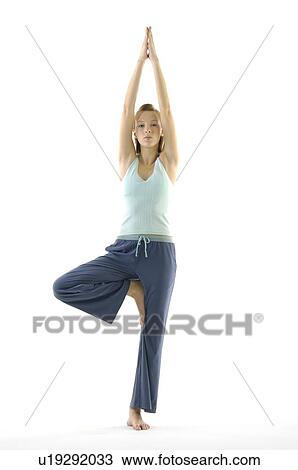 Stock Image - Portrait of a young woman standing in a tree pose. Fotosearch