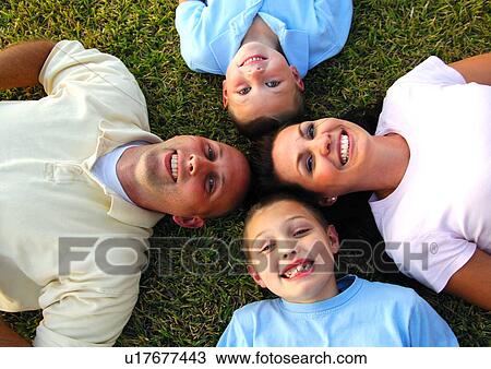 Stock Image - High angle view of a mid adult couple lying on grass in a circle with their two sons. Fotosearch