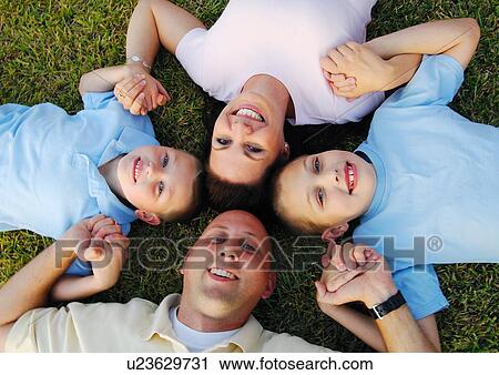 Stock Image - High angle view of a mid adult couple lying on grass in a circle with their two sons. Fotosearch