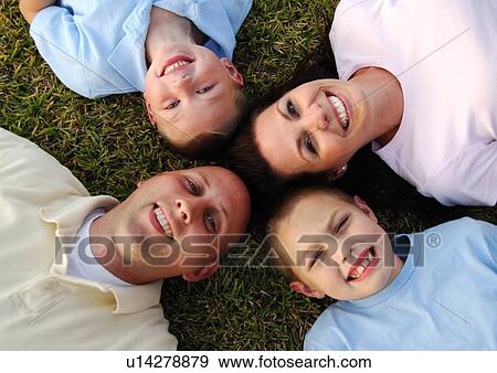 Stock Photo - High angle view of a mid adult couple lying on grass in a circle with their two sons. Fotosearch