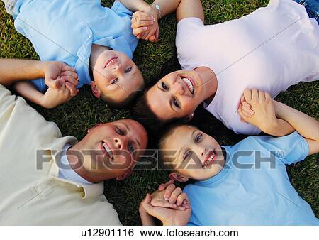 Stock Photograph - High angle view of a mid adult couple lying on grass in a circle with their two sons. Fotosearch