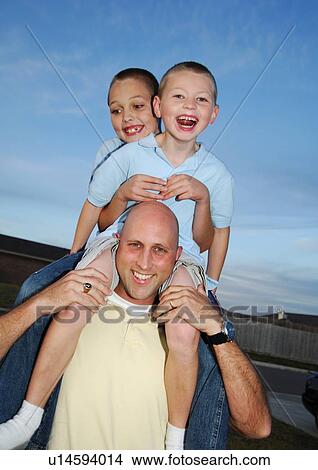 Picture - Portrait of a mid adult man carrying their two sons on his shoulders. Fotosearch