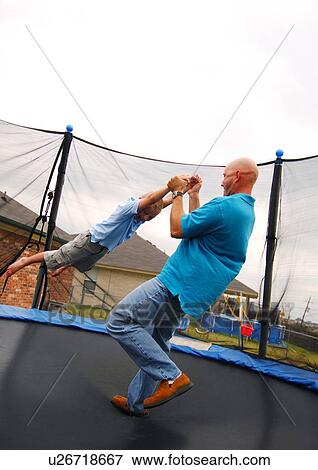 Side profile of a mid adult man playing with his son on a trampoline View Large Photo Image Stock Photo - Side profile of a mid adult man playing with his son on a trampoline. Fotosearch