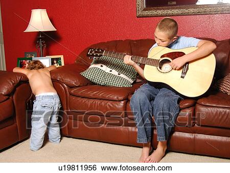 Boy playing a guitar with his sister in a living room View Large Photo Image Stock Photograph - Boy playing a guitar with his sister in a living room. Fotosearch