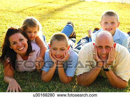 Stock Image - Mid adult couple with their children lying in a park and smiling. Fotosearch