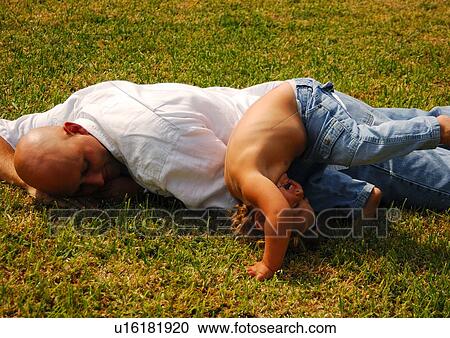 Stock Image - Mid adult man lying with his daughter in a park. Fotosearch