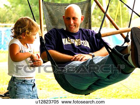 Mid adult man sitting in a hammock with his daughter standing beside him View Large Photo Image Stock Photography - Mid adult man sitting in a hammock with his daughter standing beside him. Fotosearch