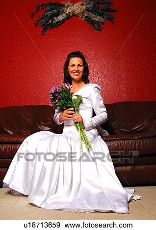 Mid adult woman sitting on a couch and holding a bouquet of flowers View Large Photo Image Stock Photo - Mid adult woman sitting on a couch and holding a bouquet of flowers. Fotosearch