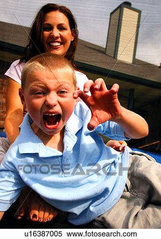 Portrait of a boy making a face with his mother sitting behind him View Large Photo Image Stock Photography - Portrait of a boy making a face with his mother sitting behind him. Fotosearch