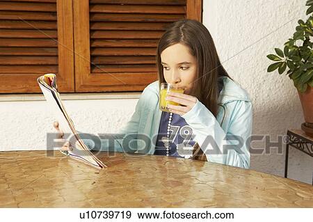 Stock Photo - Girl (12-14) drinking orange juice while reading magazine. Fotosearch