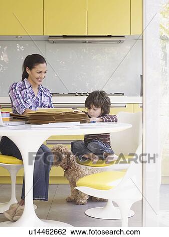 Stock Image - Woman working at home, with son at table. Fotosearch