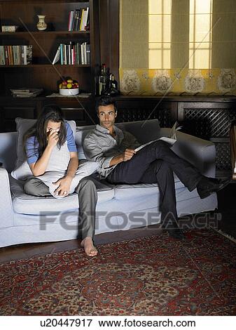 Young couple sitting on sofa illuminated by television, woman crying View Large Photo Image Stock Photo - Young couple sitting on sofa illuminated by television, woman crying. Fotosearch
