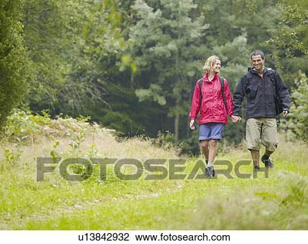 Couple walking hand in hand in a park smiling. View Large Photo Image Stock Image - Couple walking hand in hand in a park smiling.. Fotosearch