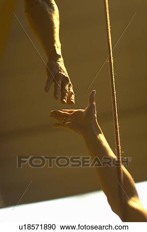Stock Image - Male climber reaching down to female climber, close-up. Fotosearch