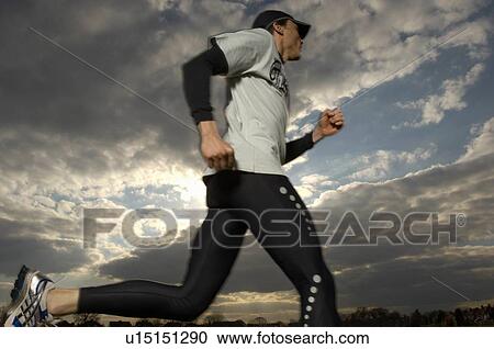 Stock Image - Male runner in park, low angle view (blurred motion). Fotosearch