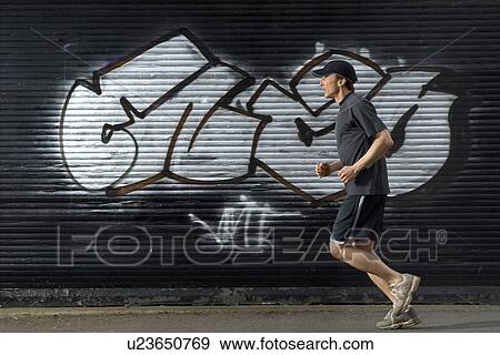 Stock Photo - Male runner passing graffiti in street, side view. Fotosearch