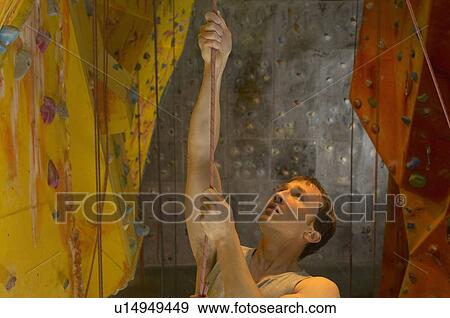 Stock Photo - Man climbing up rope at indoor climbing centre. Fotosearch