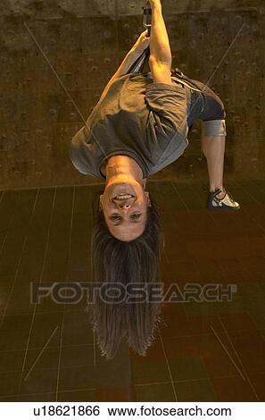 Stock Photograph - Woman hanging upside down at indoor climbing centre, smiling. Fotosearch
