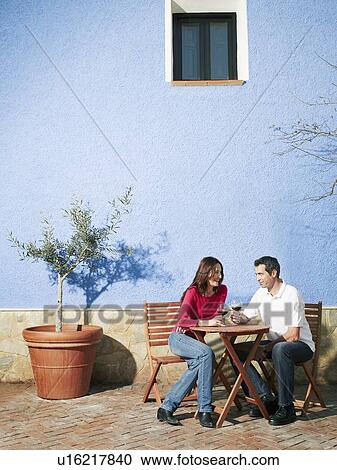 Stock Image - Couple sitting on garden terrace drinking wine. Fotosearch