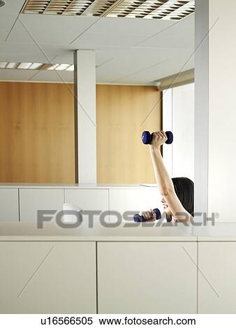 Stock Photography - Woman sitting in office lifting weights. Fotosearch