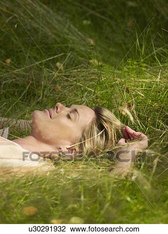 Stock Image - Woman lying in the grass sleeping.. Fotosearch