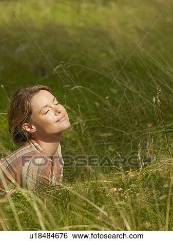 Stock Photograph - Woman lying in the grass with eyes closed smiling.. Fotosearch