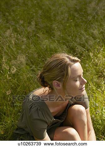 Stock Photo - Woman sitting in the grass with eyes closed.. Fotosearch