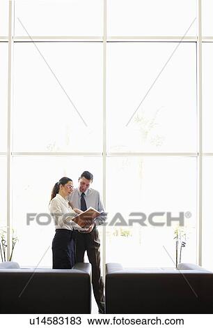 Stock Image - Businessman and woman discussing file in office. Fotosearch