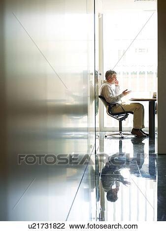 Businessman sitting in office using mobile phone, side view View Large Photo Image Stock Image - Businessman sitting in office using mobile phone, side view. Fotosearch