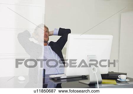 Stock Photo - Man at computer relaxing with arms behind head with reflections.. Fotosearch