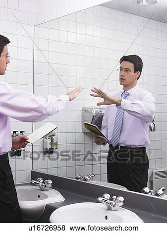 Stock Photo - Man practicing speech in office washroom mirror. Fotosearch