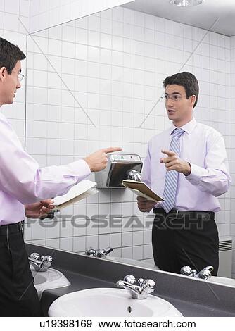 Stock Photo - Man practicing speech in office washroom mirror. Fotosearch