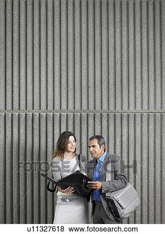 Stock Photo - Older man and young woman looking into document case against textured concrete, copy space above, Alicante, Spain,. Fotosearch