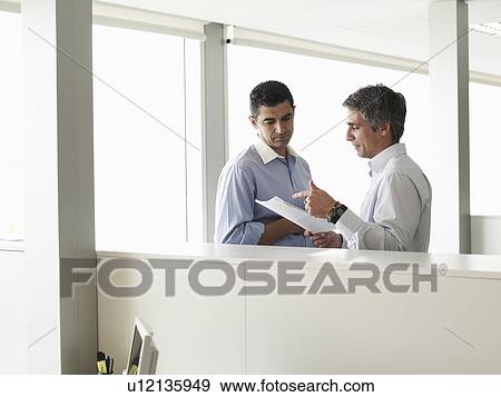 Stock Photo - Two businessmen discussing file in office. Fotosearch