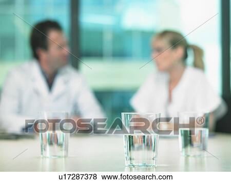 Two doctors in a business meeting. Out of focus. Close up on glasses of water in foreground. View Large Photo Image Stock Photo - Two doctors in a business meeting. Out of focus. Close up on glasses of water in foreground.. Fotosearch