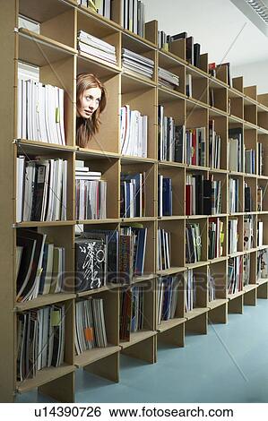 Stock Photograph - Woman peeping head through bookshelf . Fotosearch