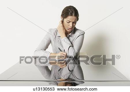 Stock Image - Young business woman at desk with reflections.. Fotosearch