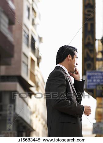 Stock Photography - Young businessman using mobile phone in street. Fotosearch