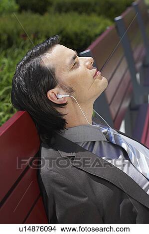 Picture - Businessman on bench with MP3 earpieces listening eyes closed close up.. Fotosearch