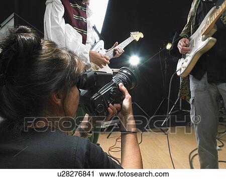 Stock Image - Female photographer shooting two electric guitar players in studio close up.. Fotosearch