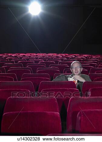 Stock Photo - Mature man eating popcorn in empty cinema. Fotosearch