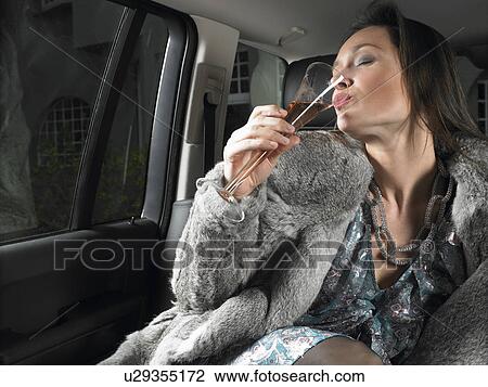 Stock Image - Woman in car, drinking and celebrating. Fotosearch