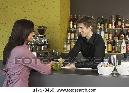 Stock Image - Young woman talking to barman. Fotosearch