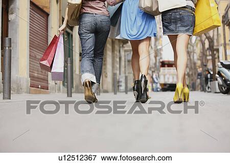 Stock Photo - Young women walking with shopping bags. Fotosearch