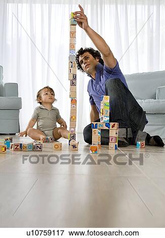 Stock Photo - Baby watching father building cube tower. Fotosearch