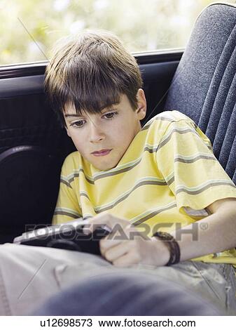 Boy (8-10) playing portable video game in backseat of car View Large Photo Image Stock Image - Boy (8-10) playing portable video game in backseat of car. Fotosearch