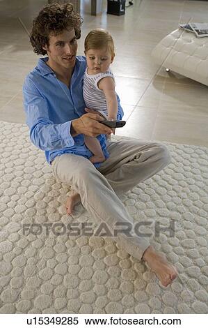 Stock Photography - Father holds baby with tv control. Fotosearch