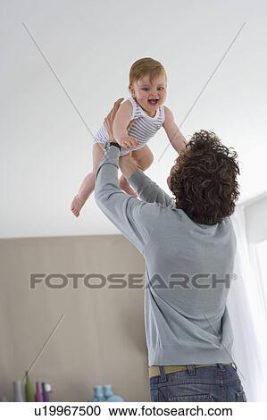 Father holds happy baby in air in house View Large Photo Image Stock Image - Father holds happy baby in air in house. Fotosearch
